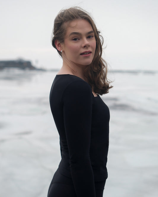 A woman wearing a black thermal long-sleeved top from the brand Skaet, standing in front of a frozen sea.