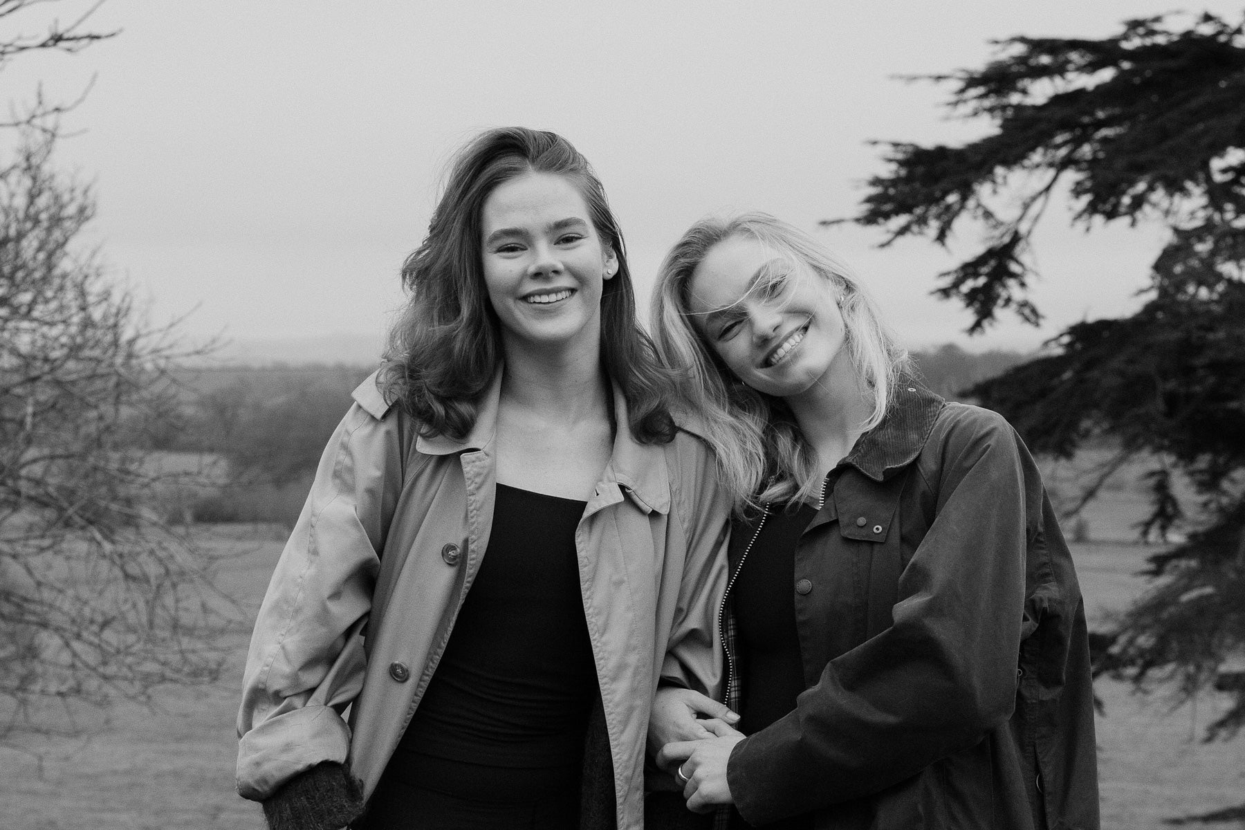 Two women standing outdoors, smiling at the camera with trees in the background