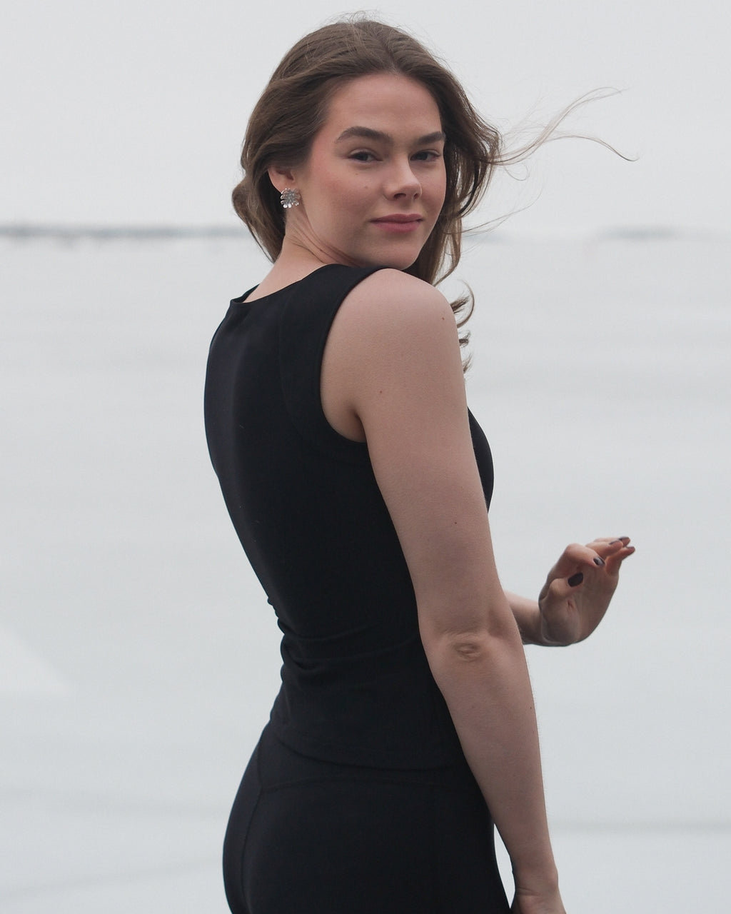 A model looking at the camera over her shoulder in the wind wearing the Skaet thermal Curve Sleeveless Top