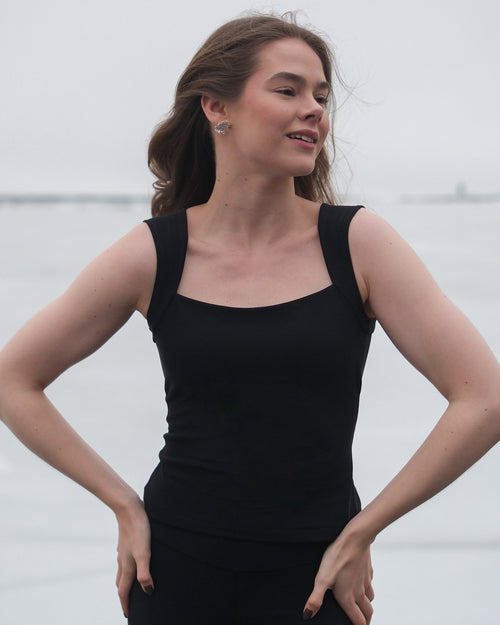 A woman wearing a sleeveless black thermal top with a square neckline and wide straps from the brand Skaet.