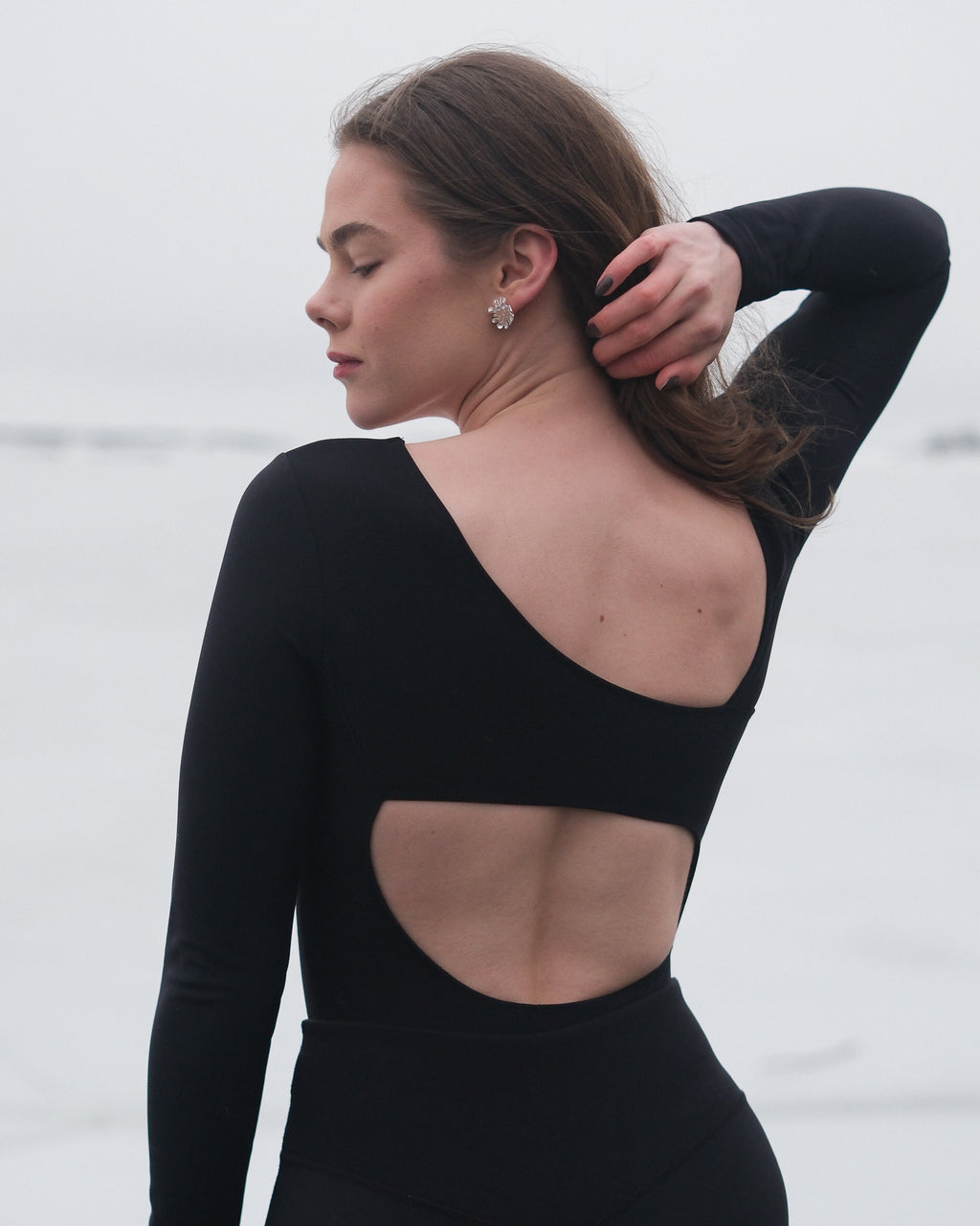 A person wearing a black long-sleeved thermal bodysuit with a cutout back detail from the brand Skaet, standing with their back towards the camera.