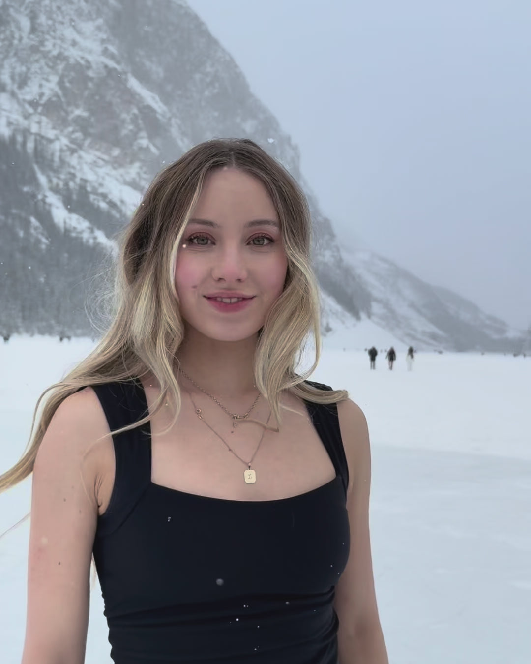 A woman ice skating on a frozen lake wearing the Skaet thermal Curve Top with mountains in the background